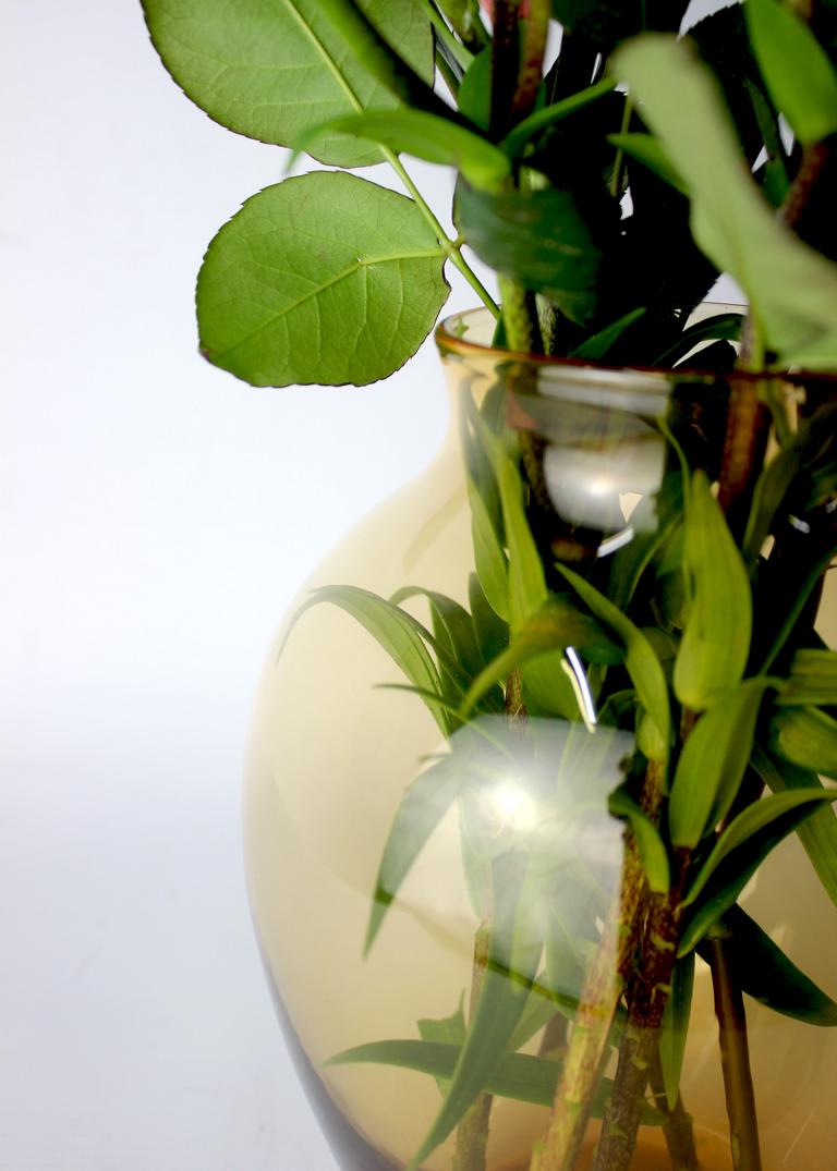 Transparente Vase in Gelb-Braun mit grünen Pflanzenstielen