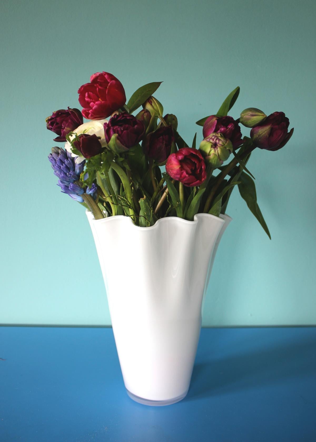 Blumenvase aus weißem Glas mit Frühlingsblumen