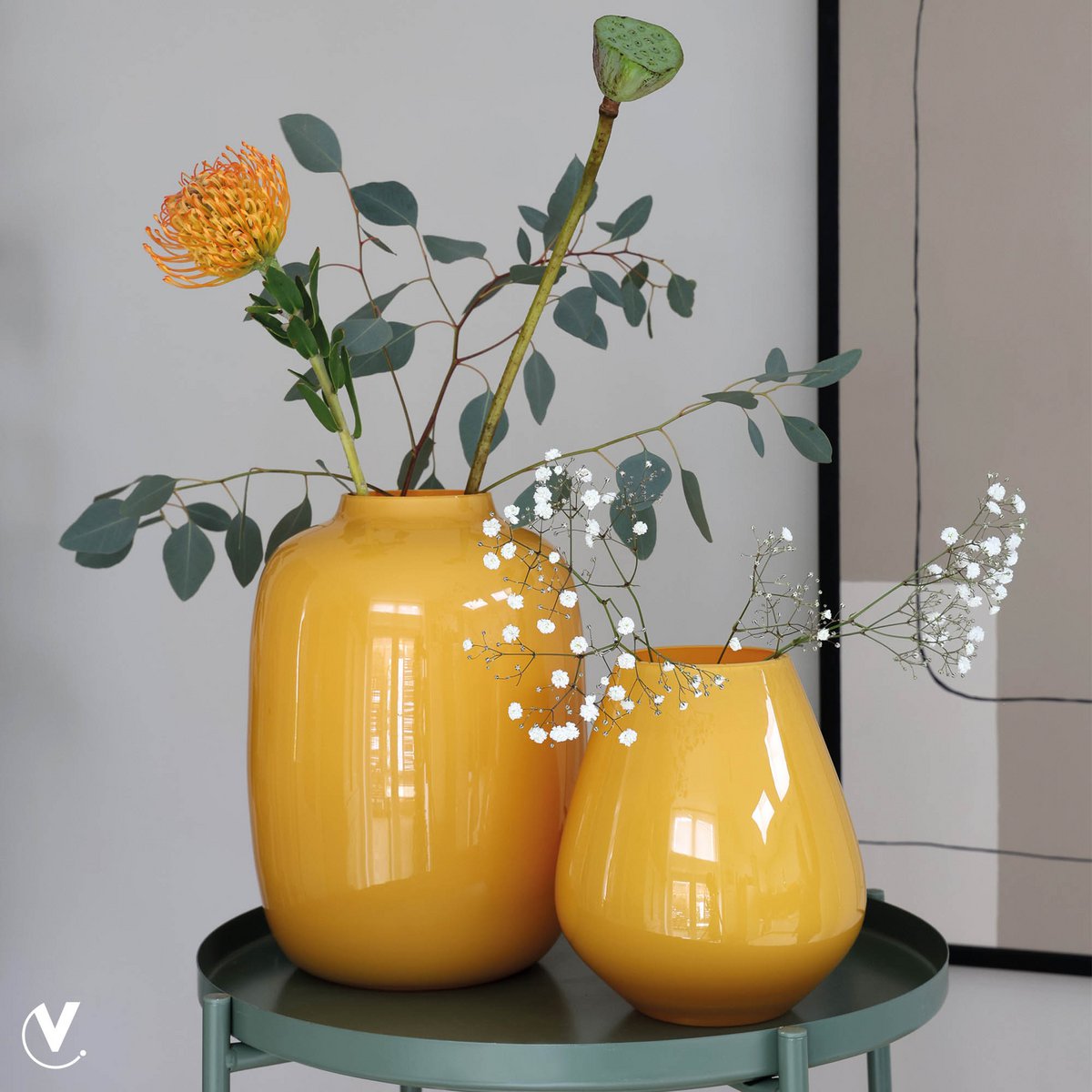 Gelbe Vase in Zylinderform auf Beistelltisch mit Gräsern und Blumen dekoriert