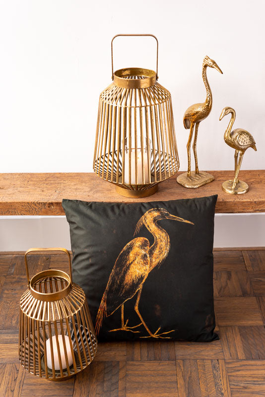 goldene Vogelfigur Kranich auf Bank mit Kissen und Windlicht