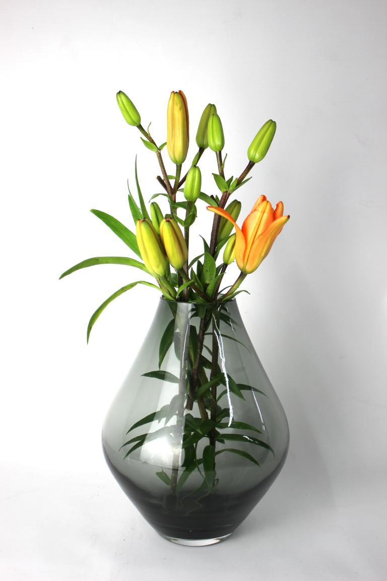 Dekorative Vase in tiefem Grauton mit grünen Lilienstängeln und leuchtender Blüte