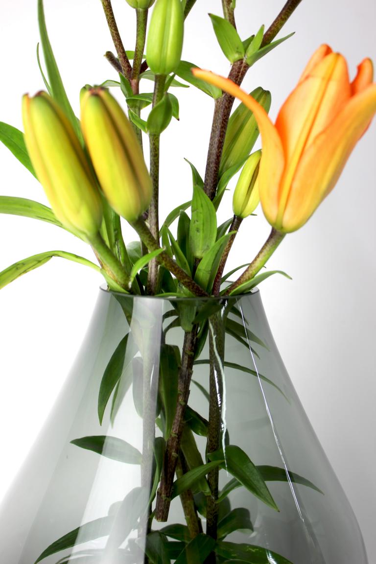 Dunkelgraue, elegante Glasvase mit orangefarbener Lilienblüte und geschlossenen Knospen