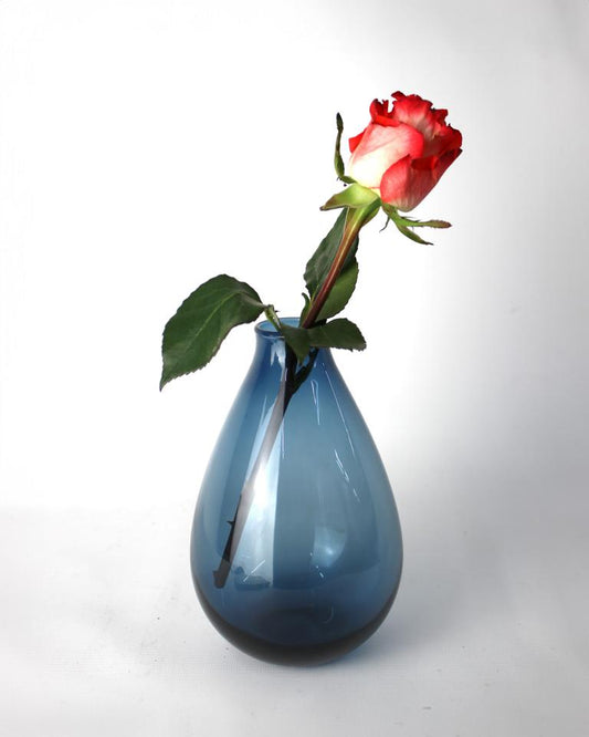 Blaue Glasvase mit leuchtend roter Rose in voller Blüte