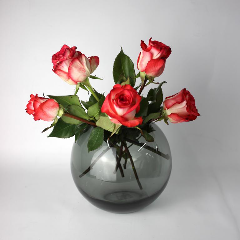 Kugelförmige Vase in Rauchfarbe mit einem Arrangement aus roten und cremefarbenen Rosen