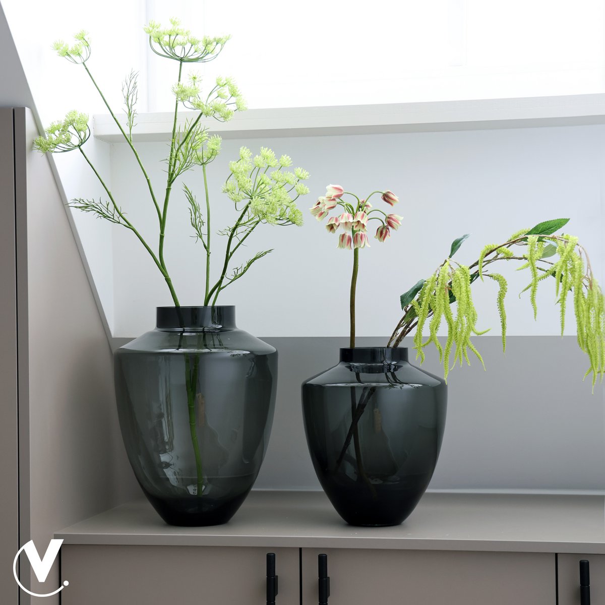 Große und kleine Glasvase in grauem Glas auf Sideboard dekoriert mit Gräsern und Blumen
