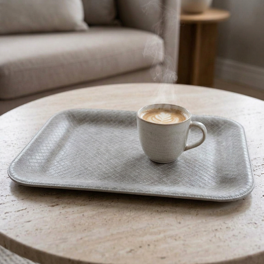 Nahaufnahme des kleinen flachen Kunstleder-Tabletts in Hellgrau mit feiner Rautenprägung und einer Kaffeetasse auf einem Couchtisch